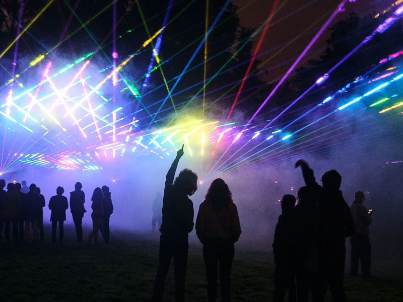 Laser show viewers silhouetted against colorful beams of lasers during Reunions.